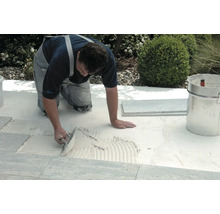 Un artisan pose des carreaux à l''extérieur avec une truelle et de la colle à carrelage.