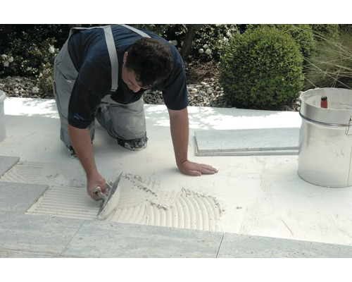 Un artisan pose des carreaux à l'extérieur avec une truelle et de la colle à carrelage.