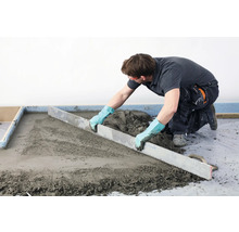 Handwerker zieht Estrich mit einer Abziehstange ab.