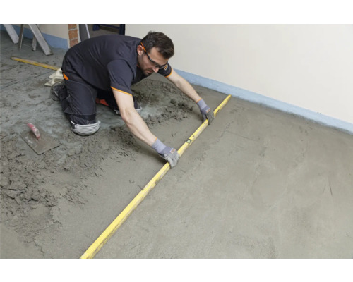 Artisan nivelant la chape avec une règle.