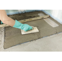 Artisan nivelant une chape dans une salle de bains à l''aide d''un niveau à bulle et d''une taloche.