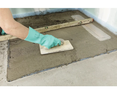 Artisan nivelant une chape dans une salle de bains à l''aide d''un niveau à bulle et d''une taloche.