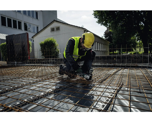 Un ouvrier du bâtiment s''agenouille sur une grille et travaille avec une meuleuse d''angle.