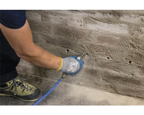 Mann reinigt Bohrlöcher in einer Wand mit Druckluft