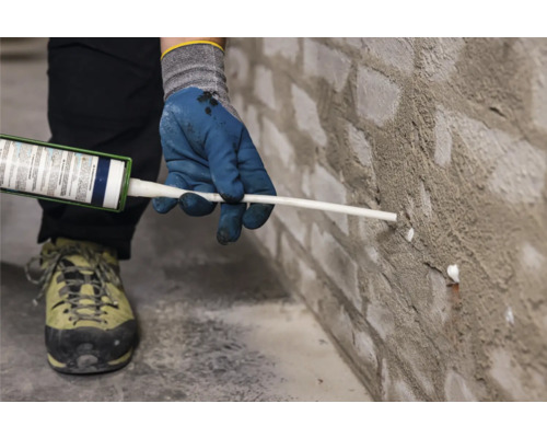 Eine Person dichtet eine Ziegelwand mit Dichtmasse ab.
