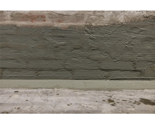 Nahaufnahme einer verputzten Ziegelwand und einem Zementboden.