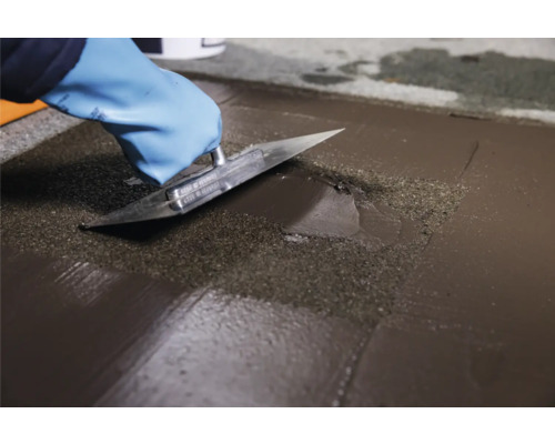 Artisan lissant un enduit de ragréage avec une spatule