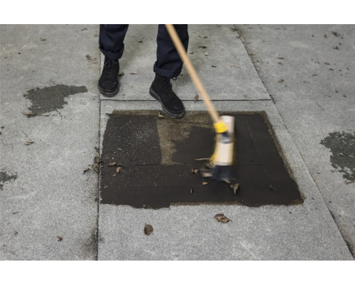 Personne nettoyant une gouttière avec un balai pour enlever les feuilles.