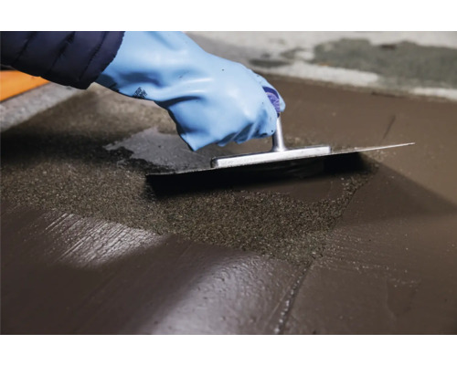 Handwerker glättet Nivelliermasse mit einer Glättkelle.