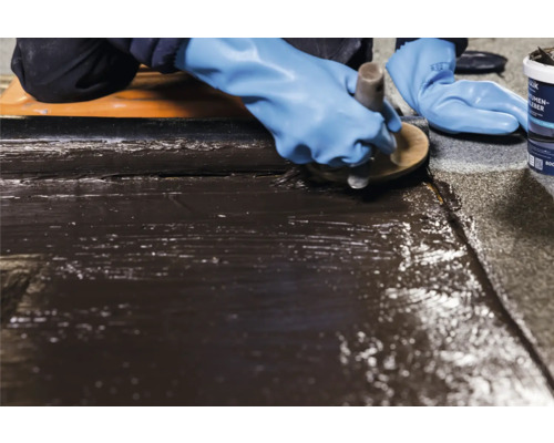 Auftragen von Bitumenkleber mit einer Bürste auf einer Oberfläche