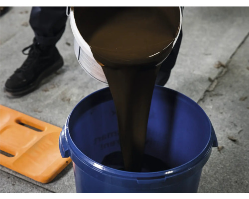 De la peinture brune est versée d''un pot de peinture dans un seau bleu.