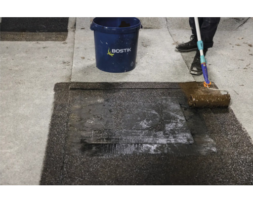 Application d''un revêtement de toiture avec un rouleau de peinture sur une surface de toit. Le logo Bostik est visible.