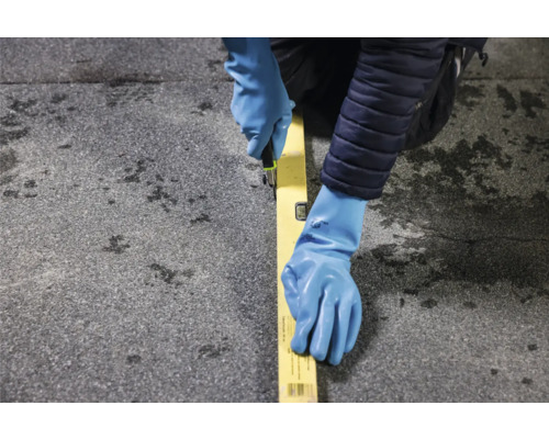 Eine Person mit Handschuhen, die mit einem Cuttermesser an einem Lineal auf einer Oberfläche schneidet