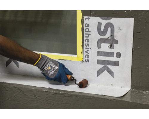 Une personne utilise un rouleau pour appliquer des bandes d''étanchéité sur une fenêtre.