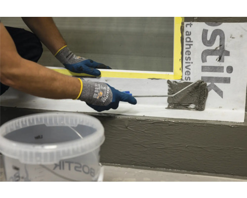 Une personne applique du mastic sur une fenêtre à l''aide d''un rouleau à peinture. Un seau de mastic est visible au premier plan.