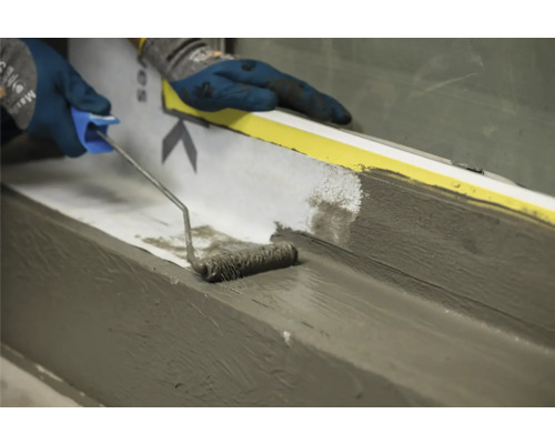 Une personne applique du mastic avec un rouleau à peinture sur une surface.