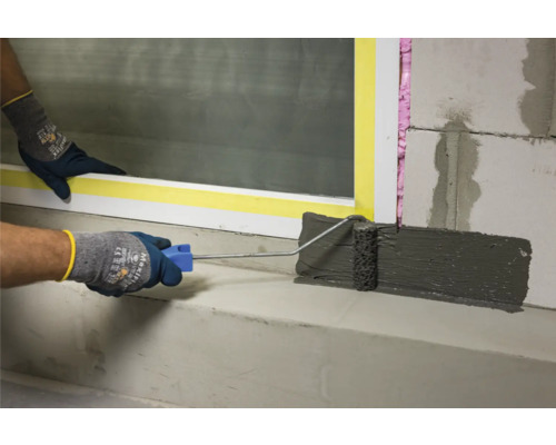 Auftragen von Dichtschlämme mit Farbroller auf einem Untergrund aus Betonsteinen