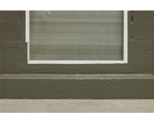 Detailansicht eines Kellerfensters mit Betonwand und Sockelleiste