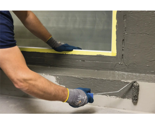 Person trägt mit Farbroller eine Abdichtung auf eine Wand auf.