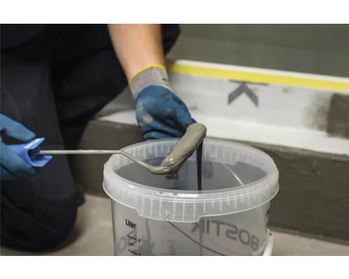 Eine Person taucht eine Farbwalze in einen Eimer mit Flüssigkunststoffabdichtung von Bostik ein.