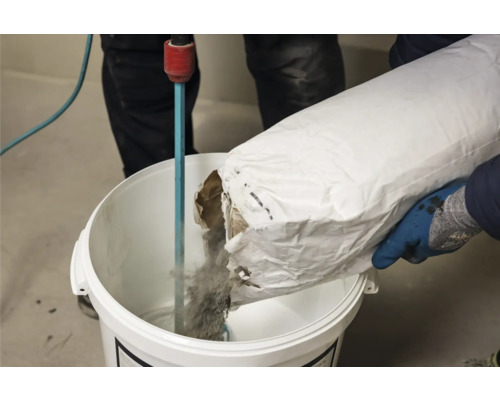 Eine Person giesst Material aus einem Sack in einen Eimer mit einem Rührwerk.