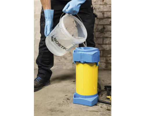 Ein Handwerker gießt Wasser aus einem Eimer in eine gelbe und blaue Vorrichtung zum Mischen von Estrich.