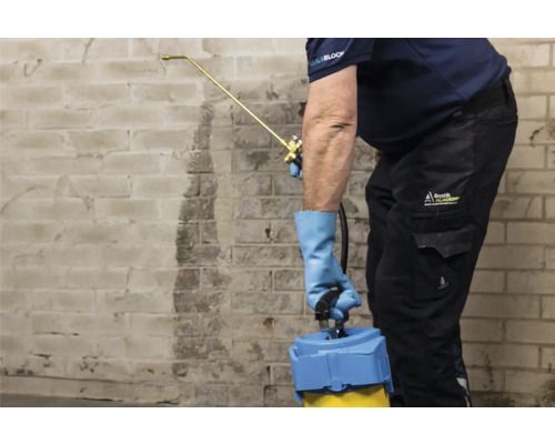 Mann sprüht mit einer Sprühflasche eine Wand ein.