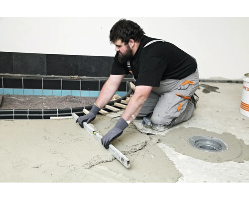 Handwerker nivelliert Estrich mit einer Wasserwaage im Badezimmer.