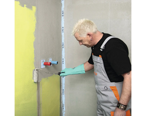 Un artisan applique un enduit d''étanchéité au rouleau sur le mur de la salle de bains.