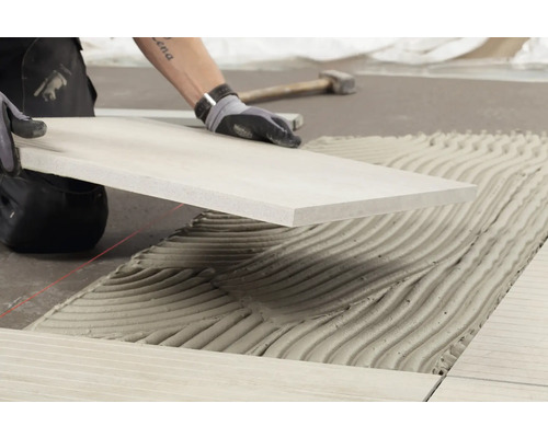 Carreleur au travail : pose de carrelage avec de la colle à carrelage.