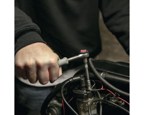 Une personne utilise un cliquet avec une douille sur un moteur.