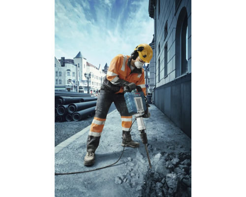 Un ouvrier du bâtiment portant des vêtements de protection utilise un marteau-piqueur pour casser du béton.