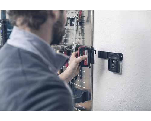 Person befestigt Akku an Pro-Click-Wandhalterung in Werkstatt