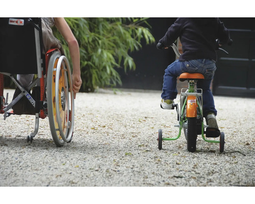 Un enfant en fauteuil roulant et un enfant sur un tricycle roulent sur une surface de gravier.