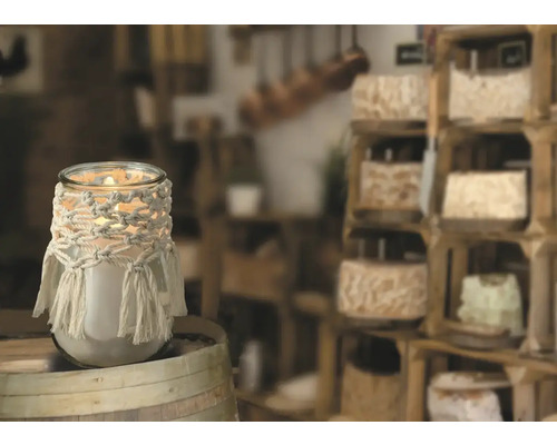 Dekorative Kerze im Glas mit Makramee-Verzierung auf Holzfass