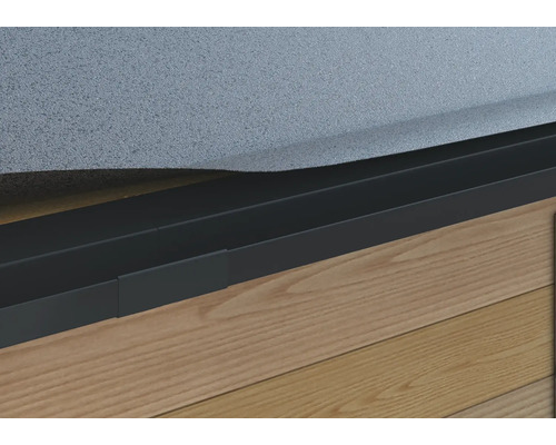 Nahaufnahme einer schwarzen Rasenkante aus Metall an einer Hauswand mit Holzboden