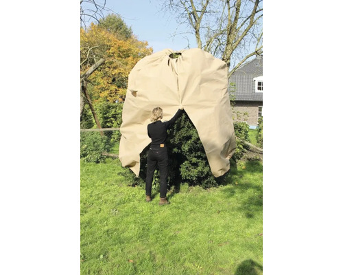 Eine Frau legt eine Pflanzenhaube über einen Strauch im Garten zum Schutz vor Kälte.