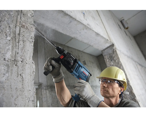 Perceuse en cours d''utilisation pour percer un mur en béton, un travailleur porte un casque de protection