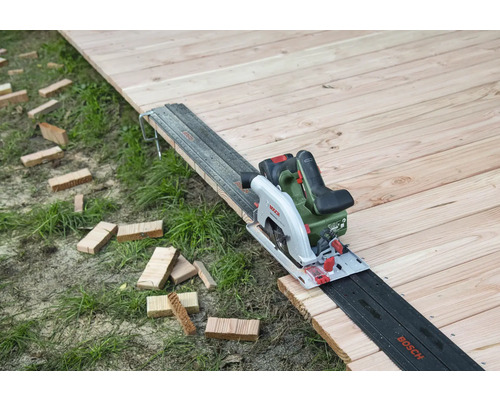 Scie circulaire à batterie sur plancher en bois avec rail de guidage et morceaux de bois