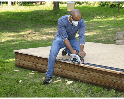 Un homme coupe une terrasse en bois avec une scie circulaire portative