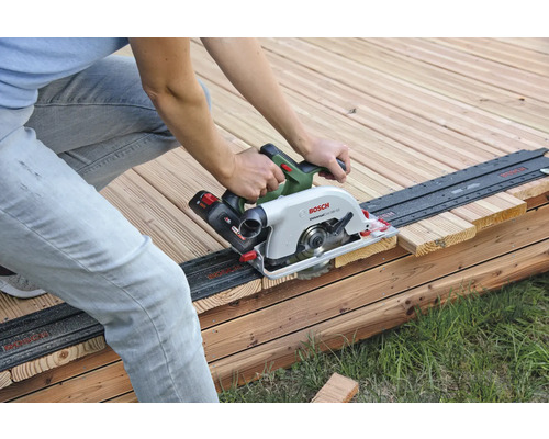 Une personne scie une planche de bois avec une scie circulaire à main sur une terrasse en bois.