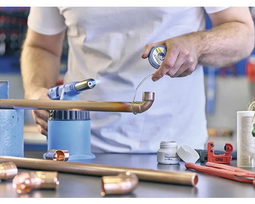 Handwerker lötet Kupferrohr mit Lötlampe und Lötzinn