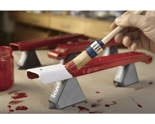 Pinceau appliquant de la peinture rouge sur une pièce posée sur des supports de pièce