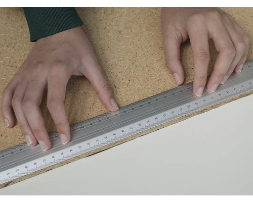 Une personne utilise une règle pour mesurer une planche de bois.