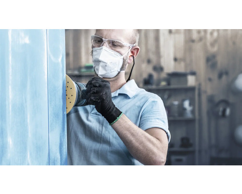 Homme ponçant du bois avec une ponceuse, des lunettes de protection et un masque respiratoire