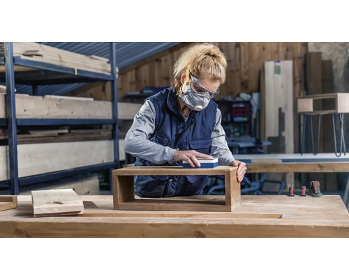 Frau schleift Holzregal in Werkstatt mit Schleifklotz