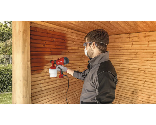 Mann lackiert Holzwand mit Farbsprühsystem