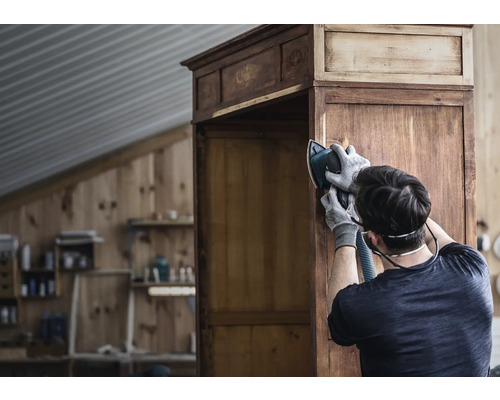 Un homme ponce une armoire en bois avec une ponceuse dans un atelier