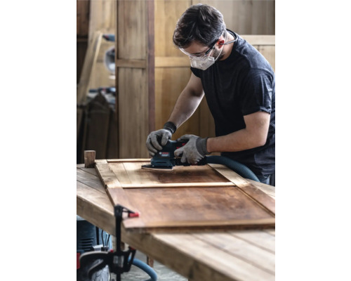 Mann schleift Holztür mit einem Schwingschleifer