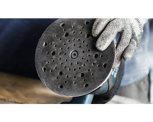 Ein Handschuh hält einen Schleifteller mit Löchern.